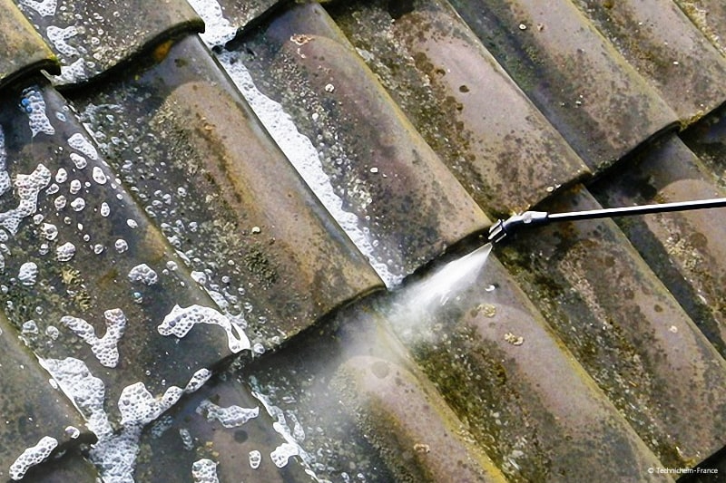 Application du produit décapant sur une toiture en tuiles béton verdies avec le temps